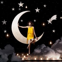 a woman in yellow dress sitting on the moon with stars and clouds above her head