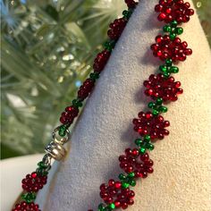 a red and green beaded necklace sitting on top of a white cloth next to a christmas tree