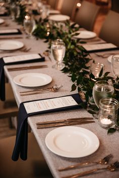 the table is set with white plates and silverware, greenery, and candles