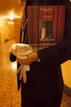 a woman holding a book in her hands and wearing white gloves on the other hand