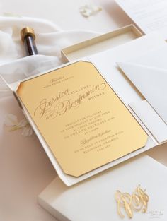 the wedding stationery is laid out on top of white paper and gold foiled envelopes