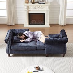 a woman laying on top of a blue couch in front of a fire place next to a white rug