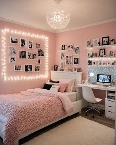 a bedroom decorated in pink and white with pictures on the wall, lights strung up above the bed