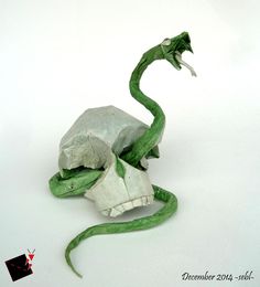 an origami sculpture of a green snake wrapped around a piece of white paper