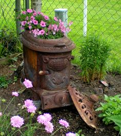 an old stove with flowers growing out of it in front of a fenced area