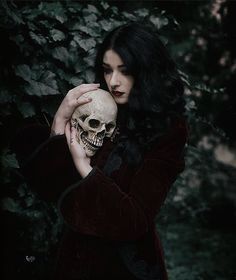 a woman holding a skull in front of her face and wearing a red coat with black sleeves