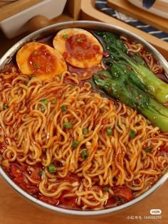 a large metal bowl filled with noodles and veggies on top of a wooden table