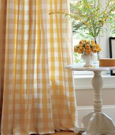 a yellow and white checkered curtain hanging in front of a window next to a table with flowers on it