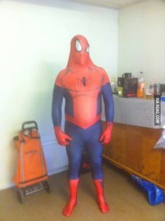 a man in a spiderman costume standing next to a luggage bag and suitcases