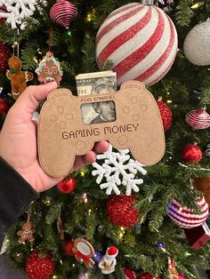 someone holding up a christmas ornament in front of a tree with ornaments on it