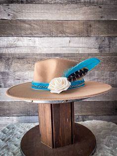 Turquoise Sahara - Camel Fedora Hat Introducing our Turquoise Sahara - Camel Fedora Hat, a regal piece put together by Bronco Western Supply. This Camel Fedora features a stunning Turquoise velvet ribbon hat band that elevates its charisma. Embellished with a rose gold chain and a beautiful cream rose, the hat captures the spirit of the wild west in an elegant way. Also included are bright turquoise and natural colored pheasant feathers that add a dash of rustic, vintage charm to the overall loo Turquoise Hats For Country Events With Short Brim, Turquoise Short Brim Hat For Country Events, Turquoise Short Brim Hat, Turquoise Curved Brim Hat For Country Events, Turquoise Wide Brim Hat For Kentucky Derby, Turquoise Brimmed Hat For Country Events, Turquoise Bohemian Fedora With Short Brim, Turquoise Hat For Kentucky Derby, Turquoise Bohemian Hat For Country Events