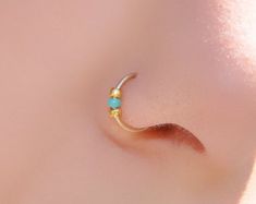 a close up view of a nose with a gold nose ring and turquoise beads on it