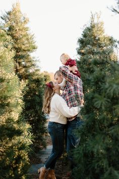 a man and woman holding a child in their arms while they stand among the trees