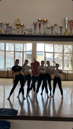 a group of people standing on top of a wooden floor next to each other in front of trophies