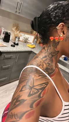 a woman with tattoos on her arm and chest sitting in a kitchen next to a counter