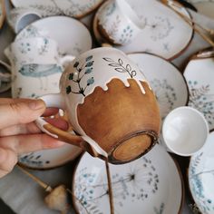 a person is holding a teapot in front of many plates with designs on them