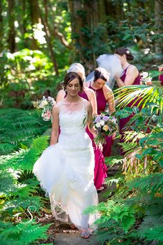 a bride and her bridal party walking through the woods