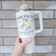 a person holding up a white travel mug with the words the beach club on it