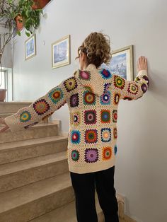 a woman standing in front of some stairs wearing a crocheted sweater and black pants