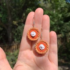 a hand holding two small orange earrings with white beads