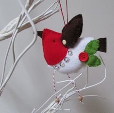 a red and white bird ornament hanging from a tree branch with green leaves