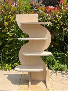 a three tiered wooden shelf sitting on top of a cement ground next to bushes