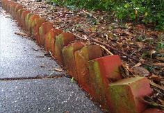 an old brick wall is lined with leaves and plants on the side of the road