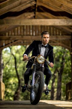 a man riding on the back of a motorcycle down a wooden road under a bridge