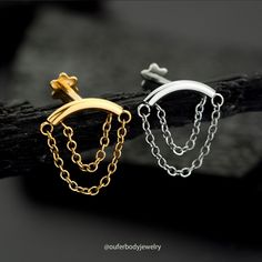 two pairs of gold and silver earrings on a piece of wood with chains hanging from it