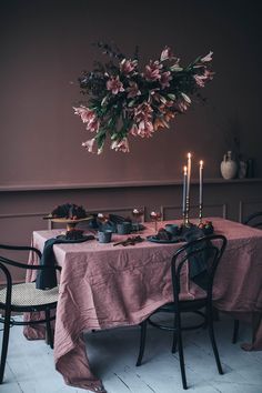 a dining room table set for two with candles and flowers hanging from the chandelier