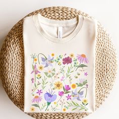 a white t - shirt with colorful flowers on it sitting next to a wicker basket