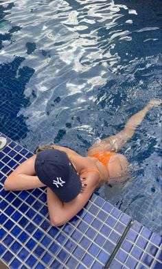 a woman in an orange bathing suit and hat sitting on the edge of a swimming pool