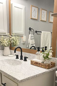 a bathroom with white cabinets and marble counter tops, black faucet, and flowers in a basket on the sink