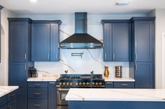 a kitchen with blue cabinets and marble counter tops, stainless steel range hood over the stove