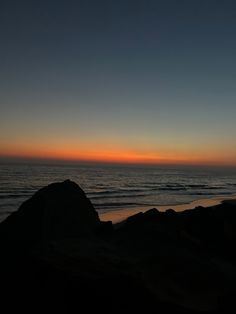 the sun is setting over the ocean and rocks