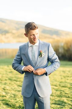 a man in a gray suit is looking down at his tie while standing in the grass