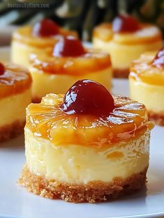 several small desserts on a white plate with pineapple sauce and cherries in the center