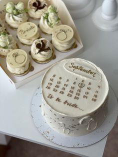 a white cake sitting on top of a table next to a box of cupcakes