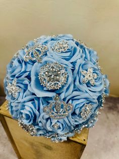 a bridal bouquet with blue roses and diable brooches on display in a gold vase