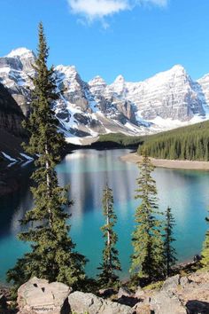 a mountain lake surrounded by snow covered mountains and pine trees in the foreground, with blue water below