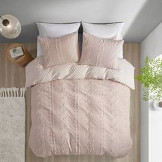 a bed with pink comforter and pillows next to a white rug on the floor