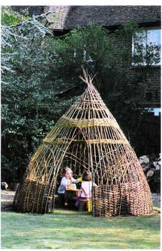 two children are sitting in front of a small wooden structure made out of sticks and branches