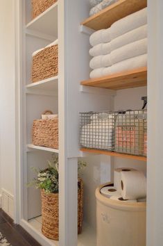 the shelves in this bathroom are filled with towels and toilet paper, along with baskets