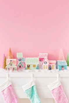 christmas stockings hanging from a mantel with houses and trees on it in front of a pink wall