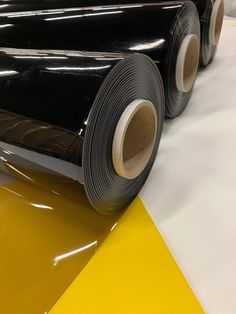 two rolls of black vinyl sitting on top of yellow and white flooring next to each other