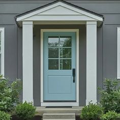 a blue front door on a gray house with white trim and windows is flanked by shrubbery