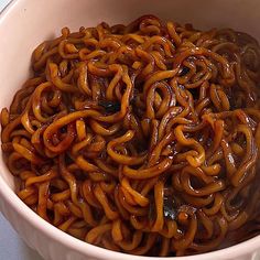 a white bowl filled with lots of brown sauce covered pasta noodles on top of a table