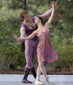 two ballerinas are performing in front of some trees and one is holding the other's hand