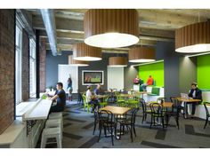 people are sitting at tables and eating in the dining area of an office building with green walls