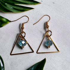 Recently worn by actress Rosa Arredondo in her role as Francey on the hit show, "So Help Me Todd", these stunning Gold Triangle Earrings, feature a mesmerizing Aquamarine glass faceted drop.  These earrings are truly an experience with golden, geometric, stainless triangles reflecting the light and capturing attention with every movement. The Aquamarine glass drop, in a beautiful, oceanic blue is the heart of these earrings, symbolizing tranquility, clarity, and elegance.  Treat yourself to the Brass Dangle Crystal Earrings For Party, Party Brass Dangle Crystal Earrings, Dangle Crystal Earrings For Party, Elegant Party Hoop Earrings With Faceted Beads, Metal Earrings With Faceted Beads For Party, Metal Earrings With Faceted Beads, Gold Faceted Crystal Earrings For Party, Faceted Brass Drop Earrings, Glass Faceted Beads Earrings For Gift